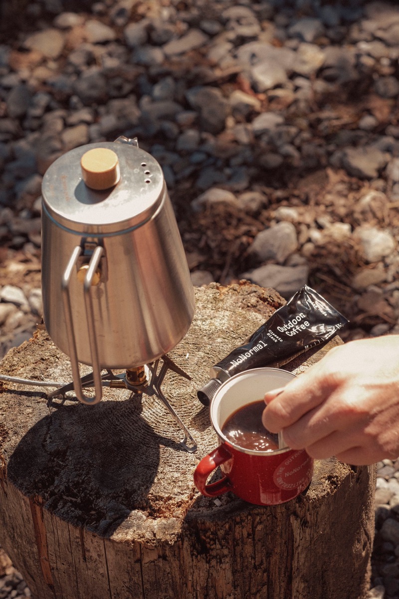 Café NoNormal préparé sur une souche, à côté d'une cafetière de camping