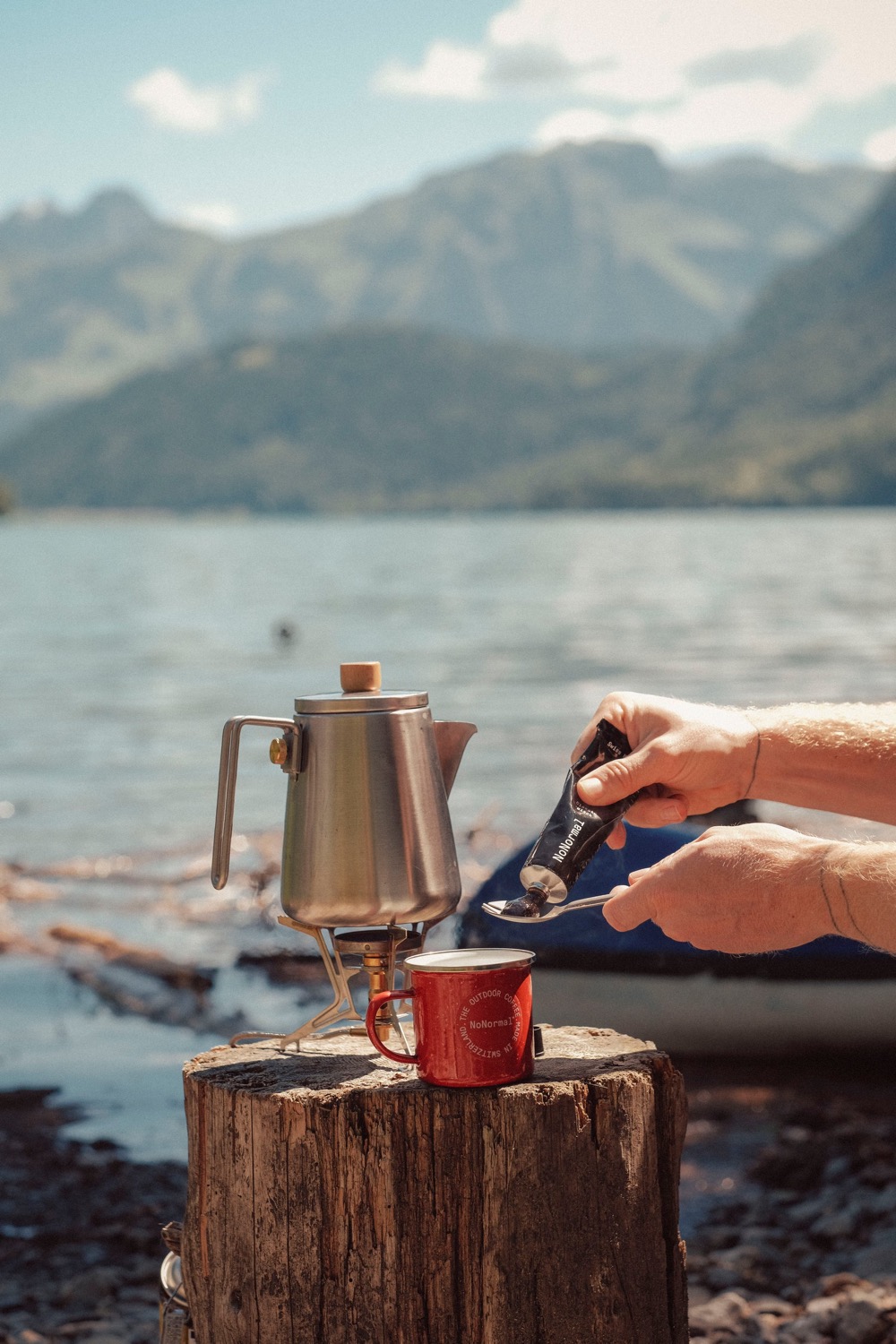 Tube NoNormal pressé au-dessus d'une tasse au bord d'un lac de montagne